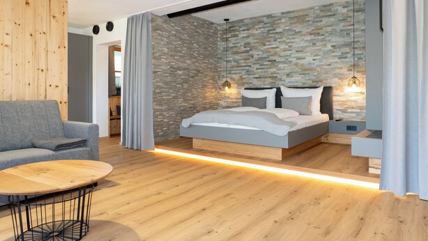 A modern bedroom with a bed, bedside tables, a sofa, and a wooden floor. - A beautiful apartment with its own terrace at Oberwinklgut. (Bischofshofen)