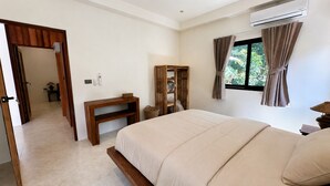 A bedroom with a bed, a wooden desk, a mirror, an air conditioning unit, and a window with curtains. - 3-Bedroom Private House in Koh Phangan – Sleeps 6 (Surat Thani)