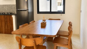 A modern kitchen with a wooden dining table and chairs, a refrigerator, and a window with blinds. - 3-Bedroom Private House in Koh Phangan – Sleeps 6 (Surat Thani)