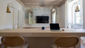 Ein Zimmer mit einem langen Tisch, zwei Stühlen, einem Laptop, einem Fernseher und dekorativen Spiegeln.
