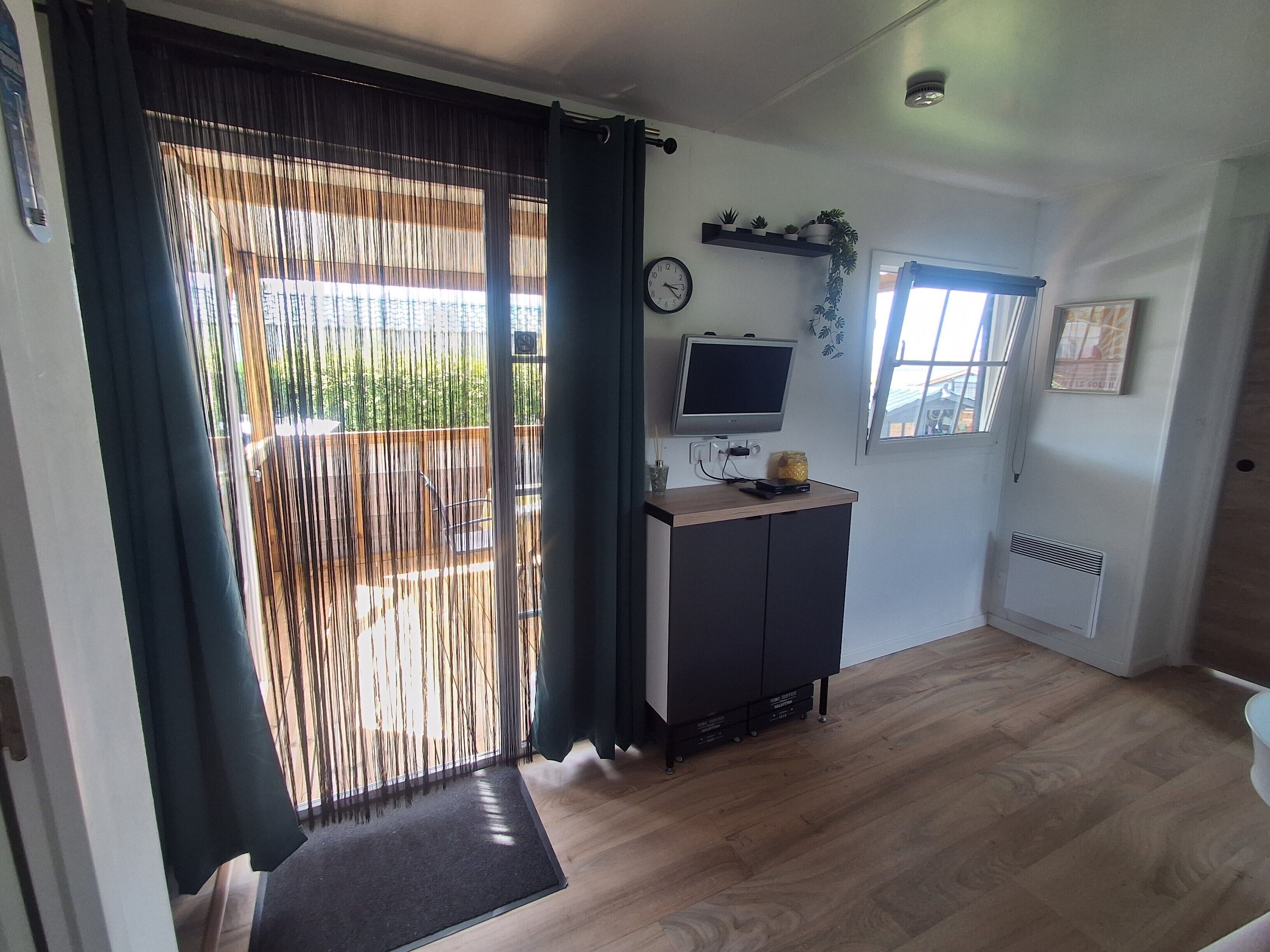 Een kamer met een schuifdeur, een klein kastje met een televisie, een klok en een raam.