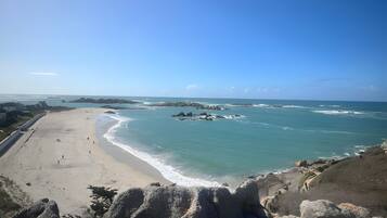 Een kuststrand met rotsformaties, een zandstrand en helderblauw water.