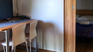 Una habitación con un escritorio de madera, dos sillas, una computadora y una cama con cabecera de madera.