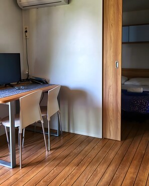 A room with a wooden desk, two chairs, a computer, and a bed with a wooden headboard.