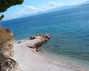 Eine felsige Küstenlinie mit klarem Wasser, ein Boot und eine Person, die auf den Felsen sitzt.