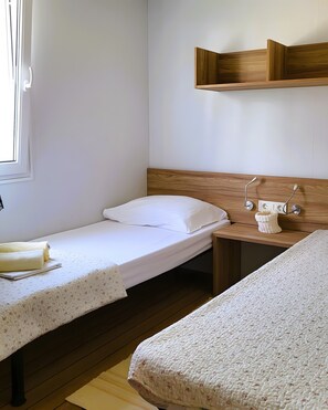 Ein Schlafzimmer mit zwei Einzelbetten, einem hölzernen Kopfteil, einem Nachttisch mit Lampe und einem an der Wand befestigten Regal.