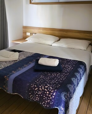 Ein ordentlich bezogenes Bett mit einer blauen, gemusterten Tagesdecke, einem weißen Kopfkissen und einem gefalteten Handtuch.