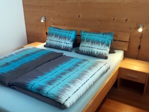 Een bed met een blauw-grijze deken, twee kussens met een blauw-grijze print, en twee bedlampjes.