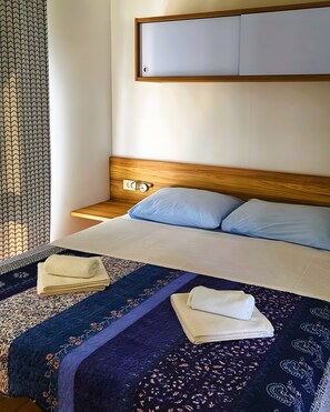 Una camera d'albergo con un letto, una testiera in legno, un comodino e una TV a parete.