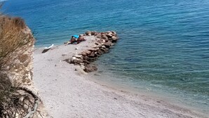 Un rivage rocheux bordé d’une eau claire, un bateau et une personne assise sur les rochers.