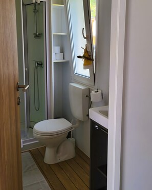 Un bagno con toilette, bidet, doccia e una finestra vista aperta sulla campagna.