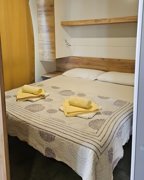 Una cama bien hecha con una colcha estampada, un cabecero de madera y una mesita de noche con una lámpara.