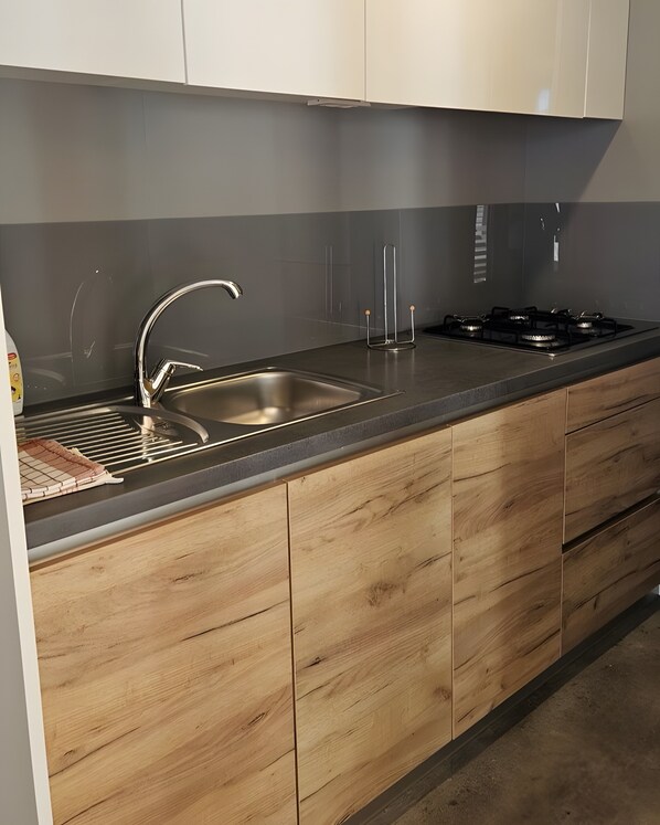 A kitchen with a stainless steel sink, a gas stove, and wooden cabinets.