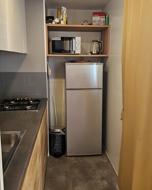 Een kleine keuken met een gasfornuis, een magnetron, een koelkast en een afvalbak.