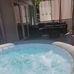 Een jacuzzi omringd door tuinmeubilair, een overdekt terras en een schuifpui.