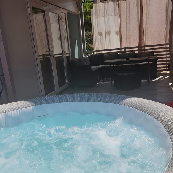 Un jacuzzi rodeado de muebles de exterior, un porche cubierto y un ventanal corredero.