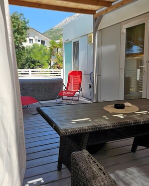 A covered outdoor area with a table, a red chair, and a wicker chair.