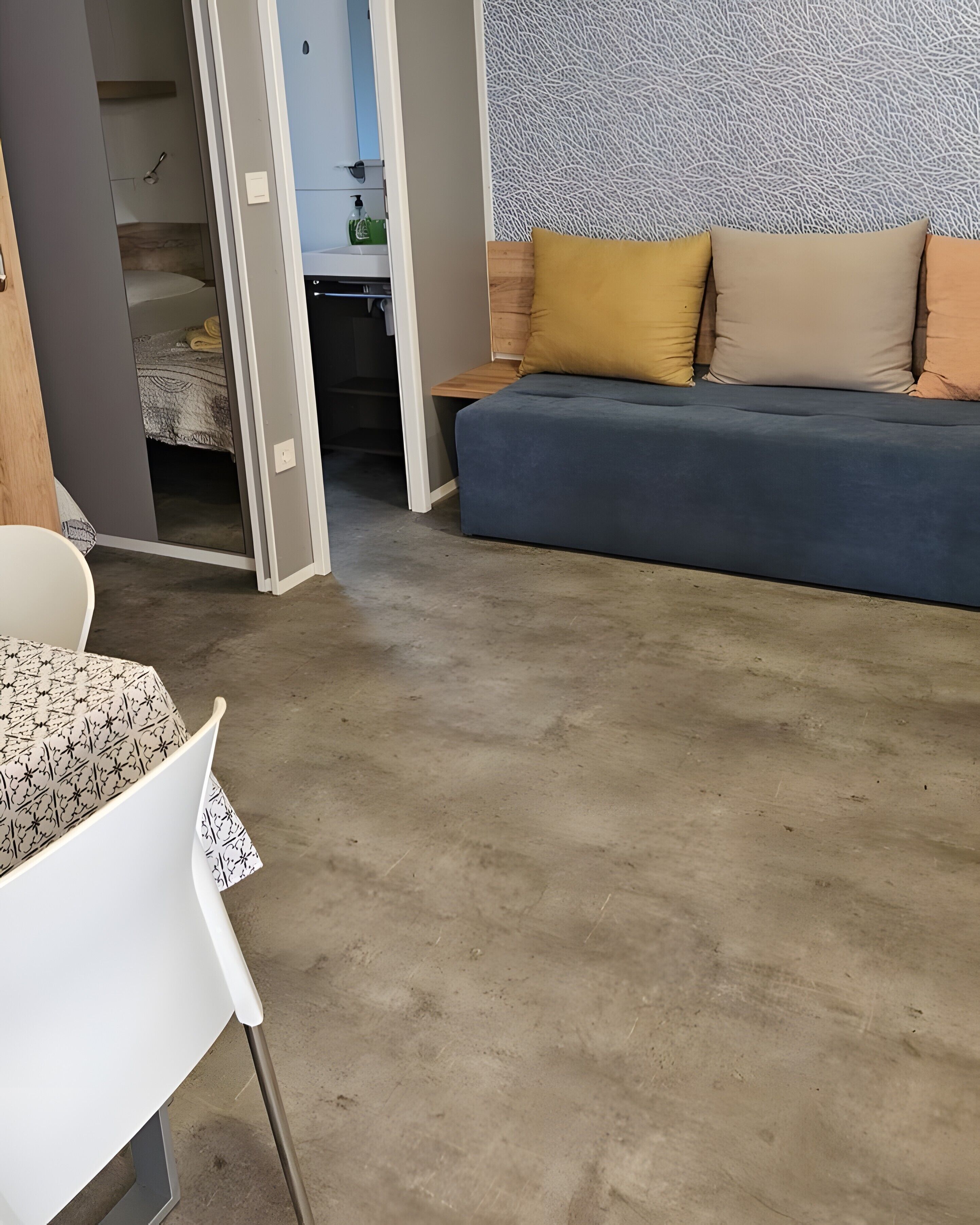 Una habitación con sofá, una mesa y una silla. Hay un armario con espejo y estante.
