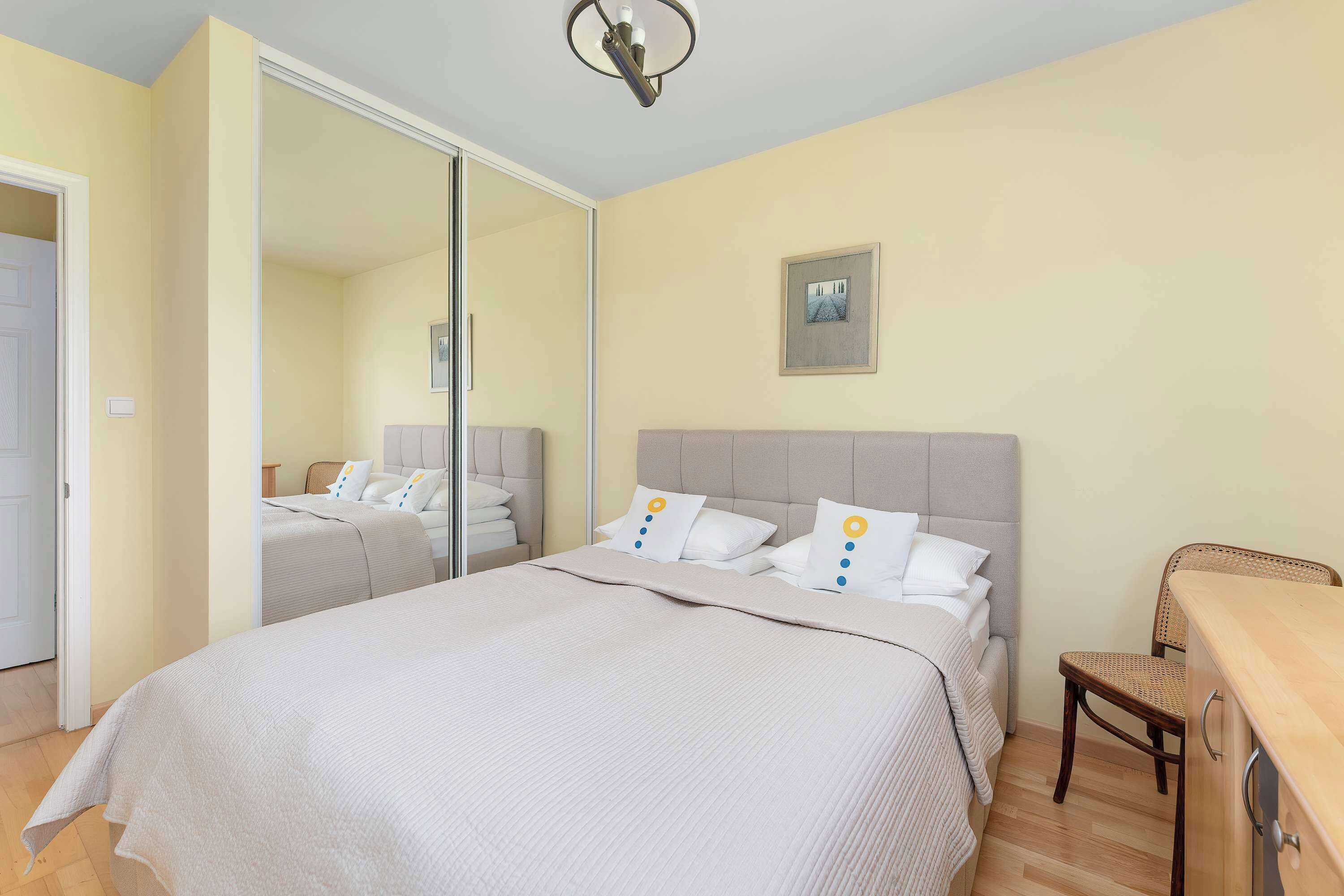 Un dormitorio con cama, una silla, un escritorio, un espejo y un cuadro en la pared.