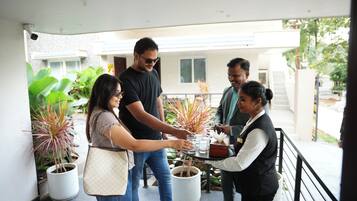 A group of people standing on a balcony with potted plants, a table with glasses and a cake, and a building in the background.