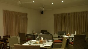 A dining area with wicker furniture, tables set for two, and a ceiling fan.