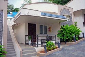 Un edificio residencial moderno con un porche cubierto, una escalera que lleva a la entrada y plantas en macetas.
