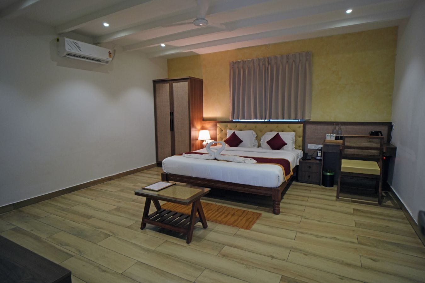 Una habitación de hotel con cama, mesita de noche, lámpara y un taburete pequeño de madera.