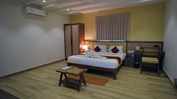 Una habitación de hotel con cama, mesita de noche, lámpara y un taburete pequeño de madera.