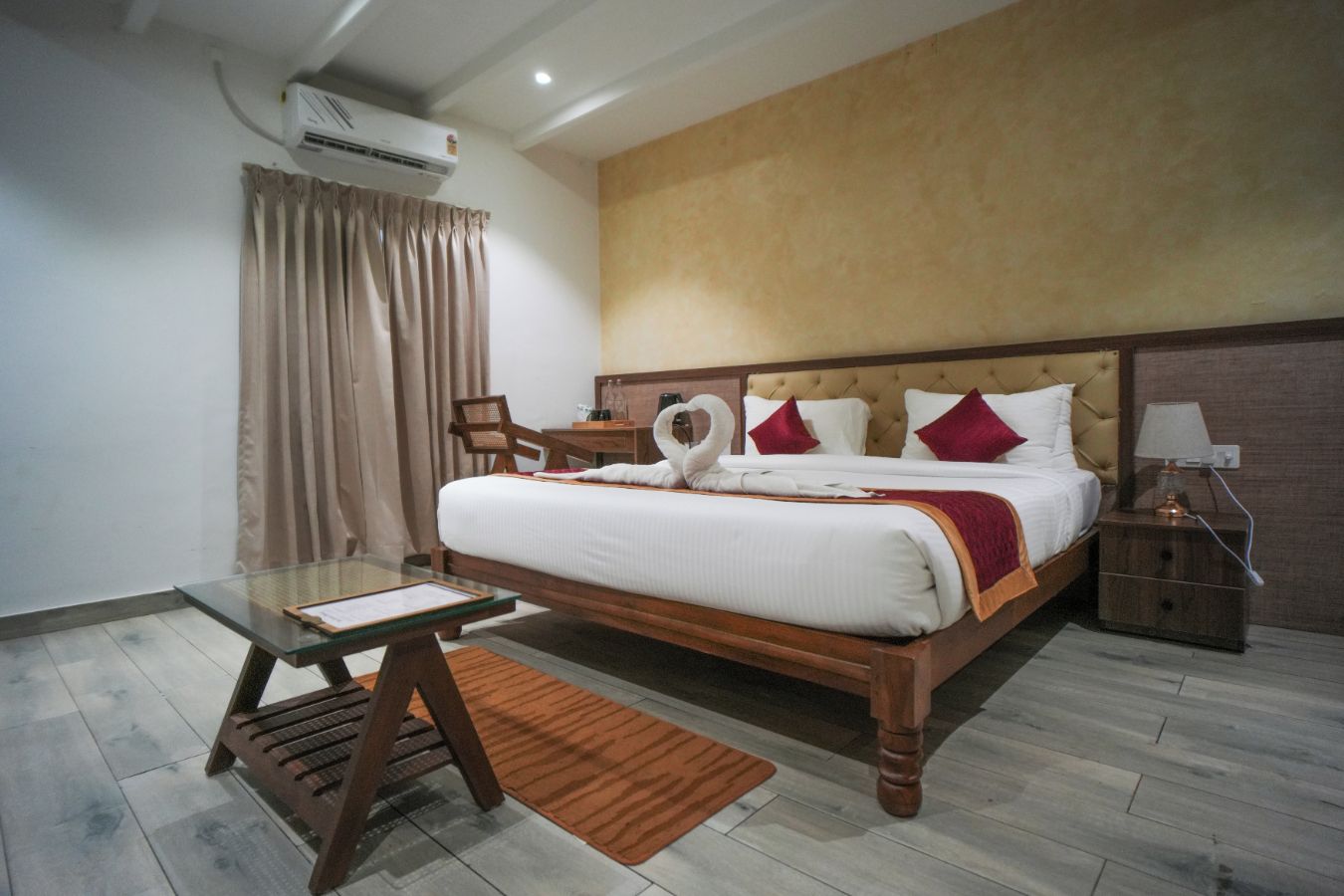 A hotel room with a bed, a desk, a chair, an air conditioning unit, and a nightstand.