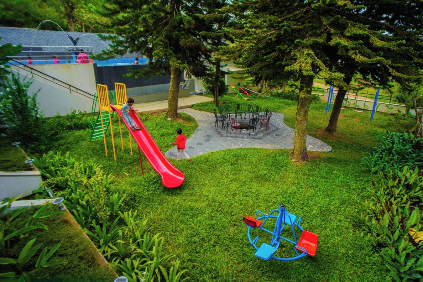 Ein Spielplatz mit einer roten Rutsche, Schaukeln und einem Tisch mit Stühlen.