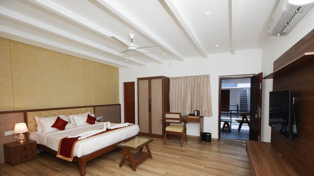 A hotel room with a bed, bedside table, chair, desk, TV, and a view of the outside.