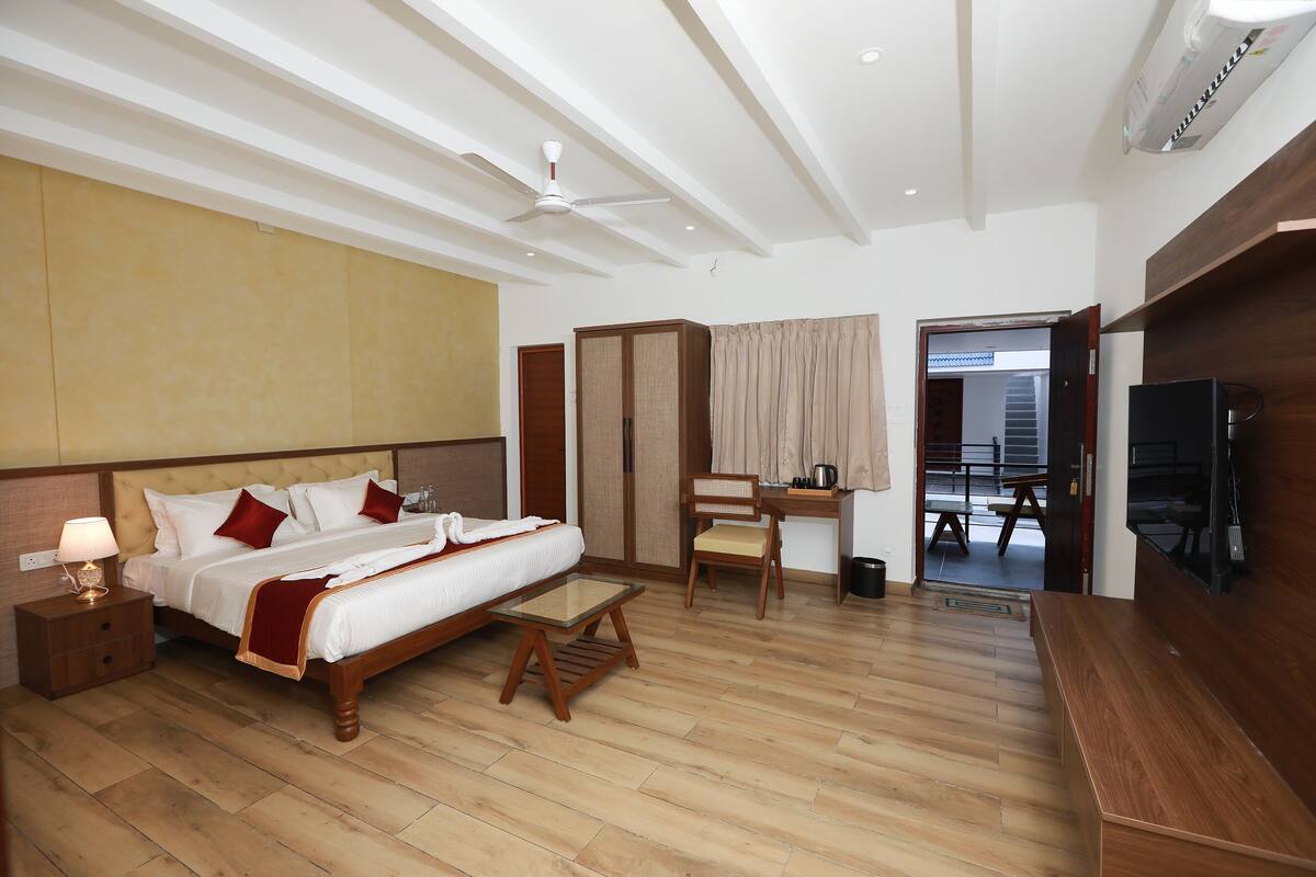 A hotel room with a bed, bedside table, chair, desk, TV, and a view of the outside.