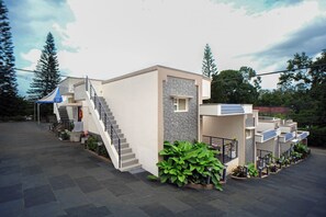 Un edificio moderno con una escalera que conduce a un balcón, rodeado de follaje y árboles.