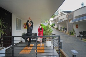 Dos personas practicando yoga sobre esterillas en un patio con macetas y un edificio al fondo.