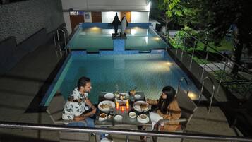 A dining area with a pool view, a table with plates and glasses, and a person seated.