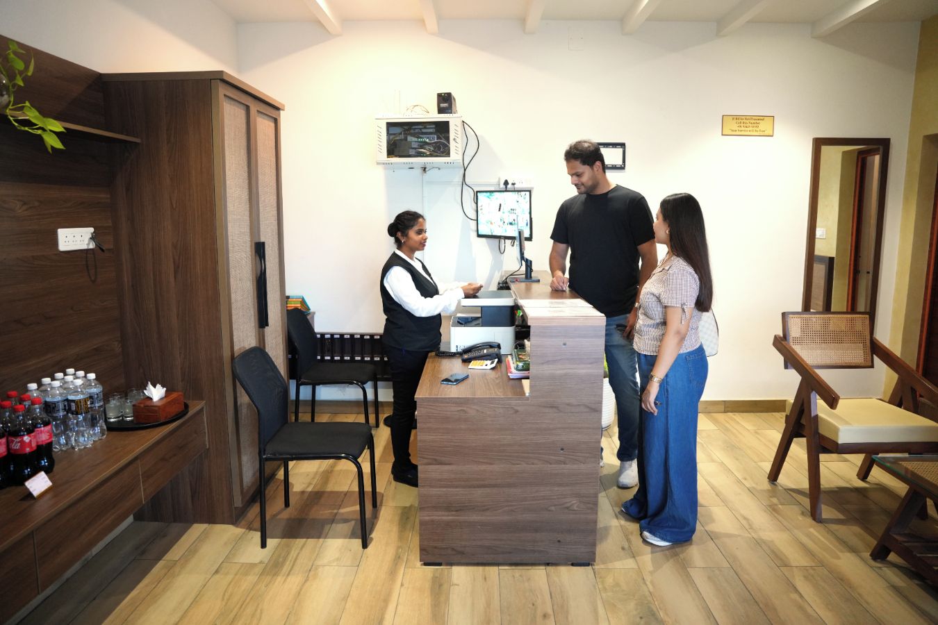 Un área de recepción con un mostrador de madera, un monitor de computadora y un teléfono. Hay sillas y un banco en la sala.