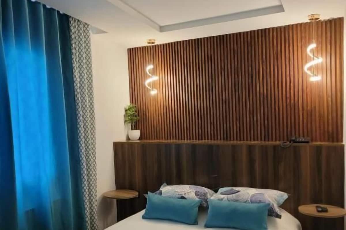 Une chambre d’hôtel moderne avec un lit, deux tables de chevet, une tête de lit en bois et un rideau bleu.
