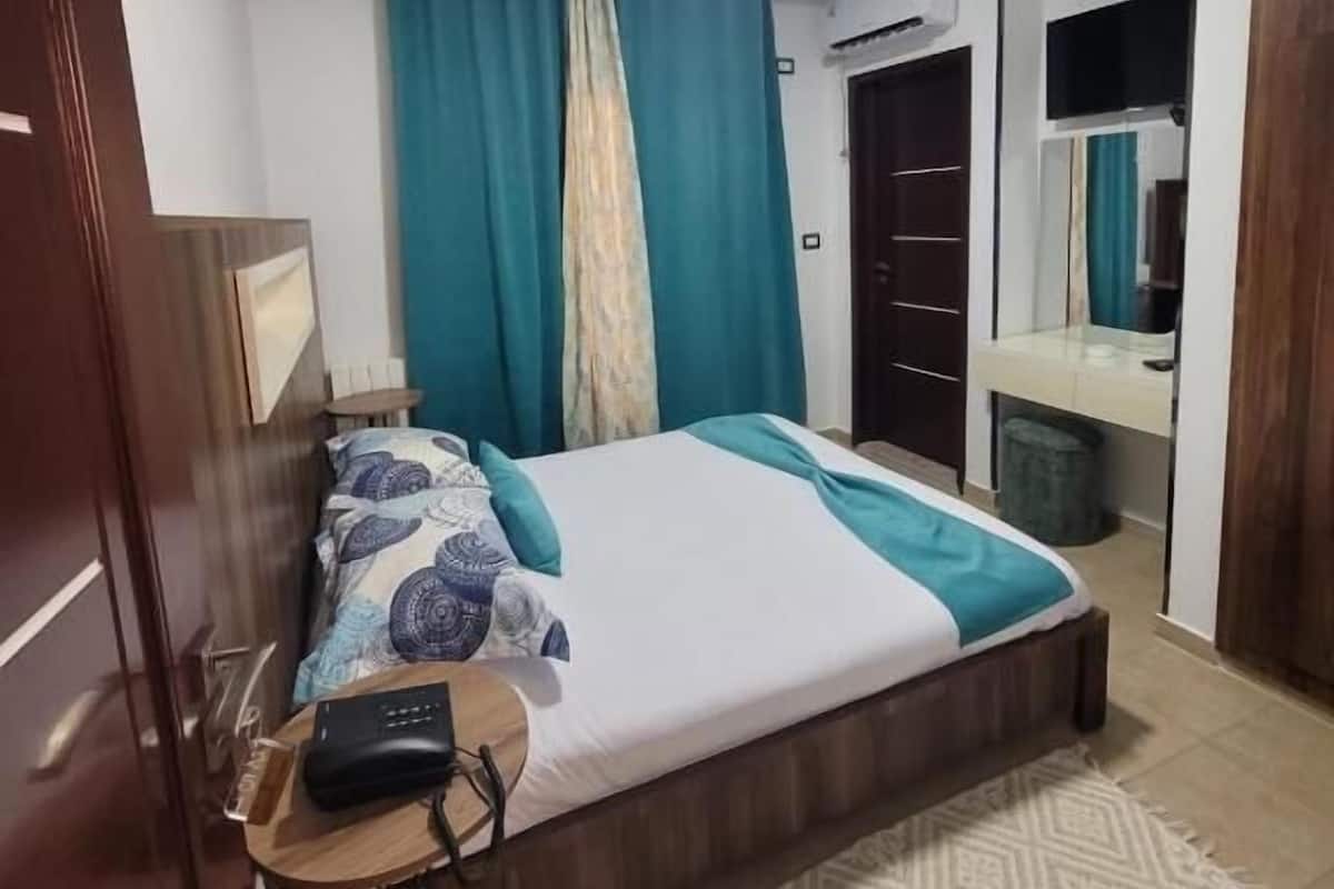 Une chambre à coucher comprenant un lit, une table de chevet, une lampe, un appareil de climatisation et un miroir.