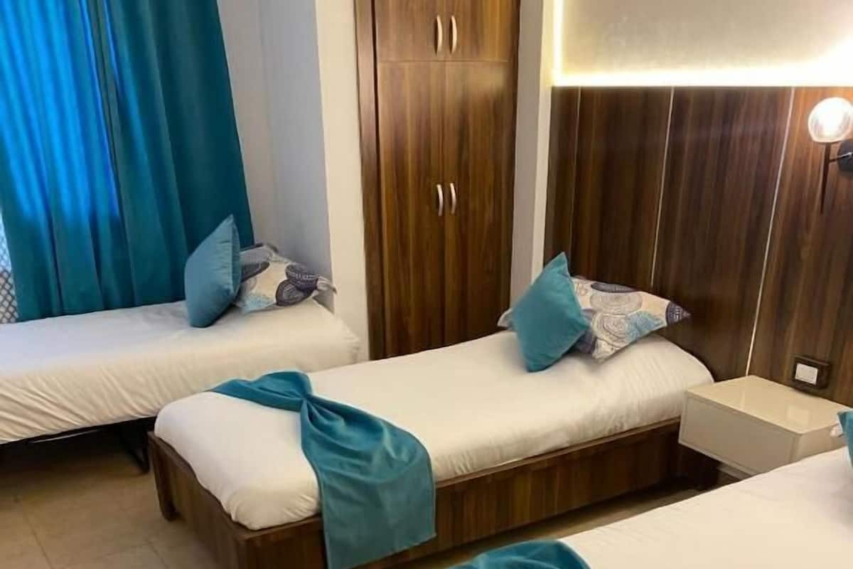 Une chambre d’hôtel avec deux lits simples, des têtes de lit en bois, une table de chevet et une lampe fixée au mur.