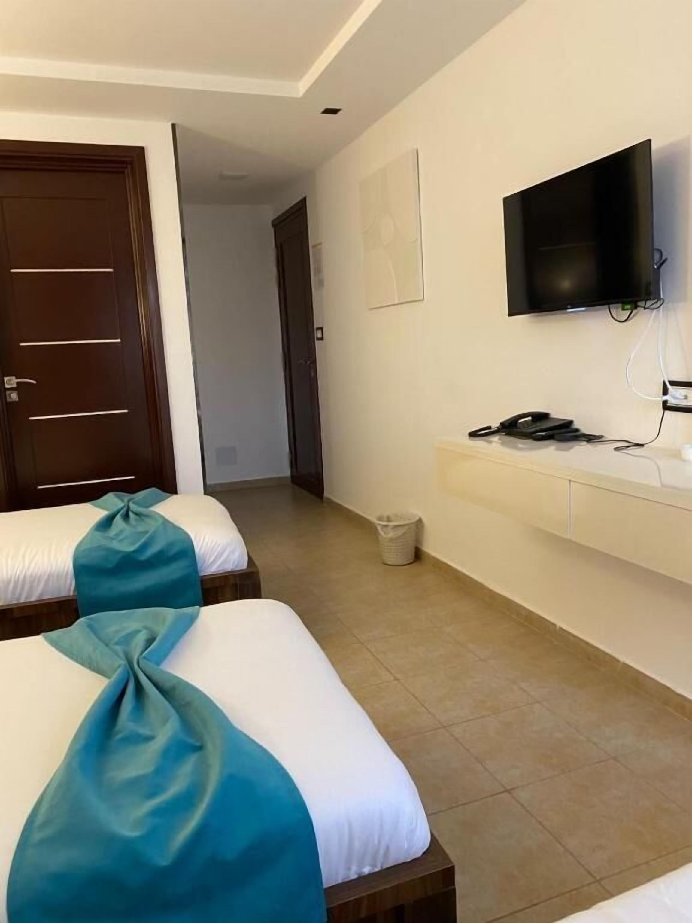 A hotel room with two beds, a TV, a desk, and a trash bin.