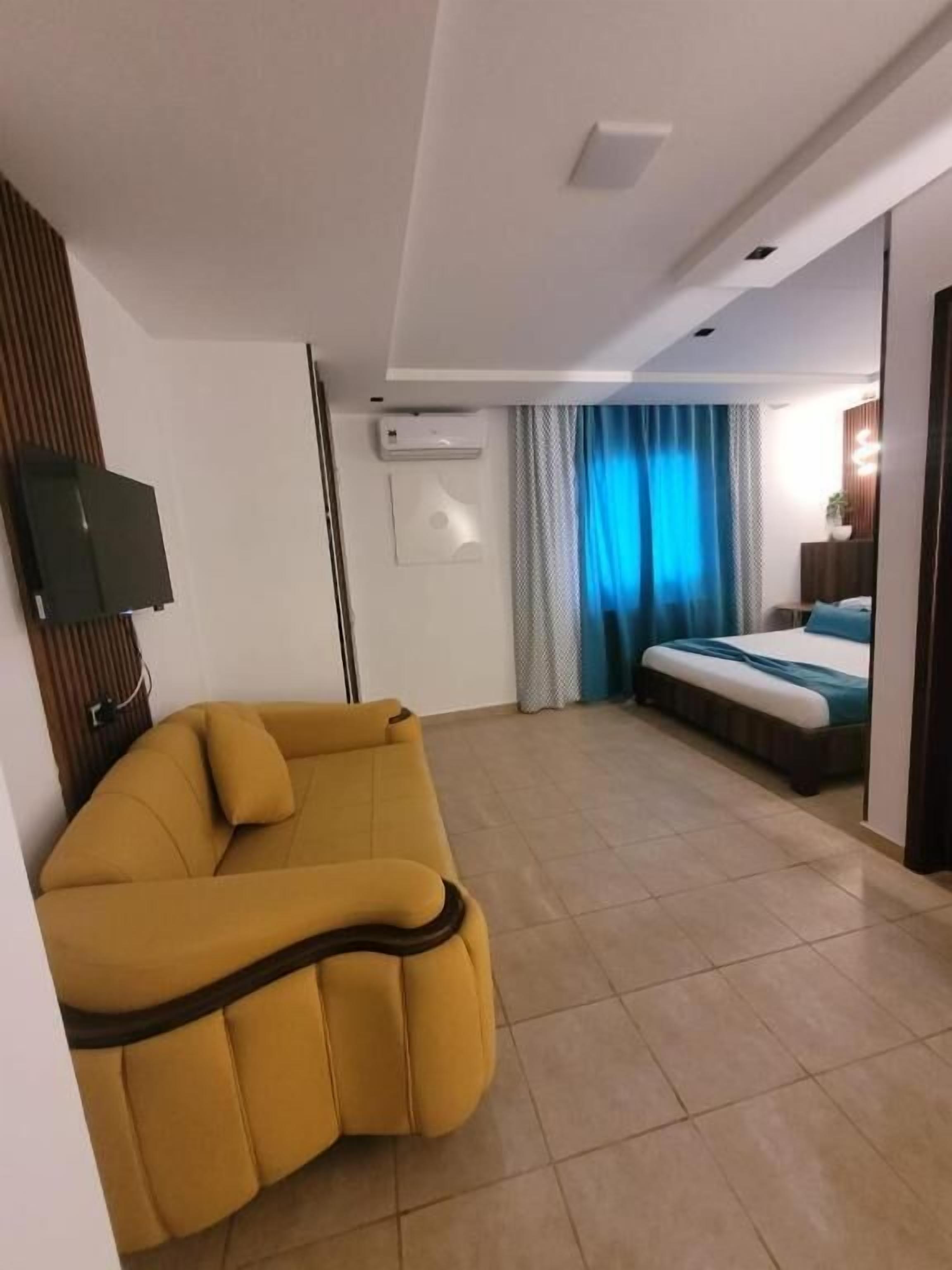 A modern hotel room with a sofa, a bed, an air conditioning unit, and a television.