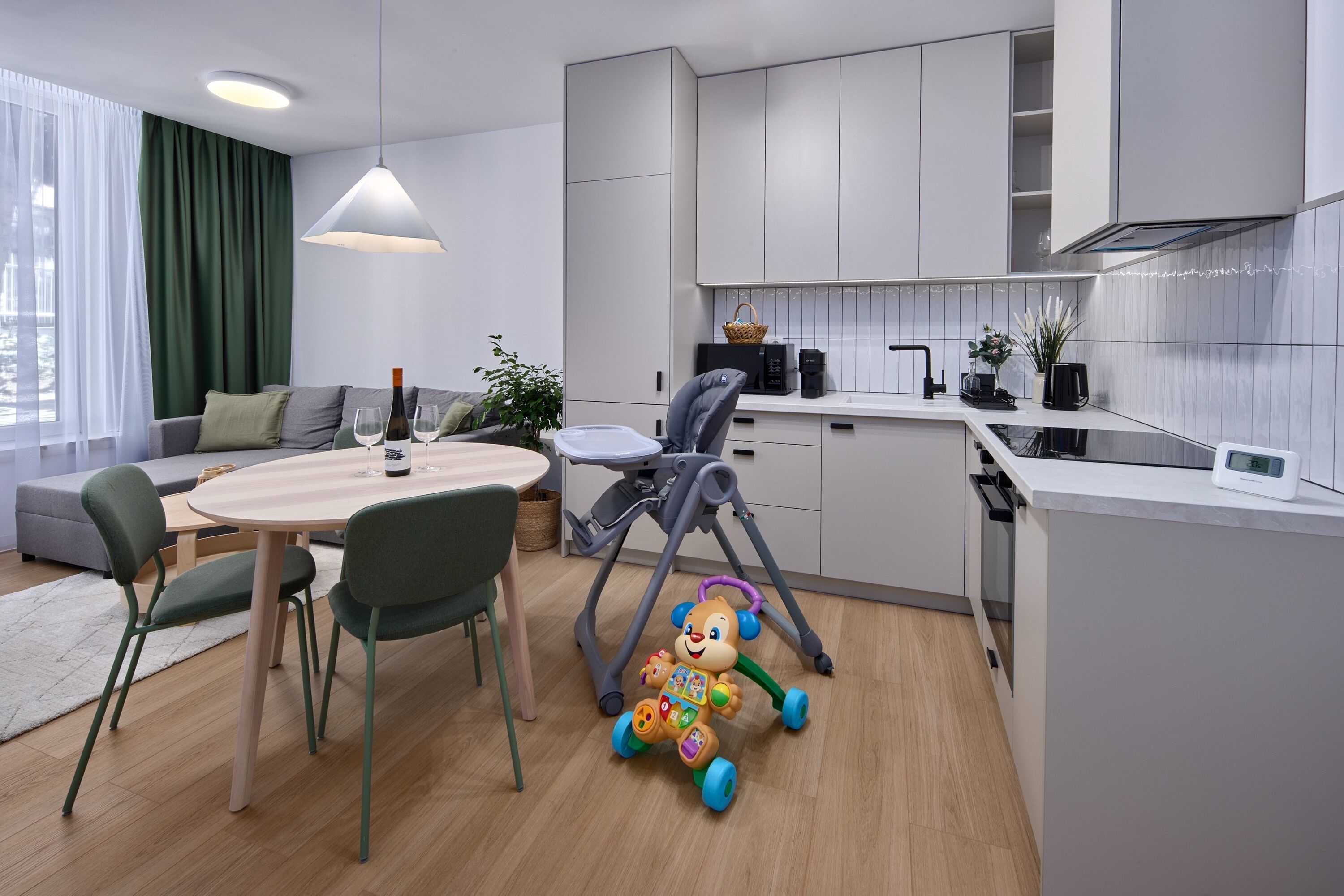 A modern kitchen with white cabinets, a dining table with chairs, and a baby walker.