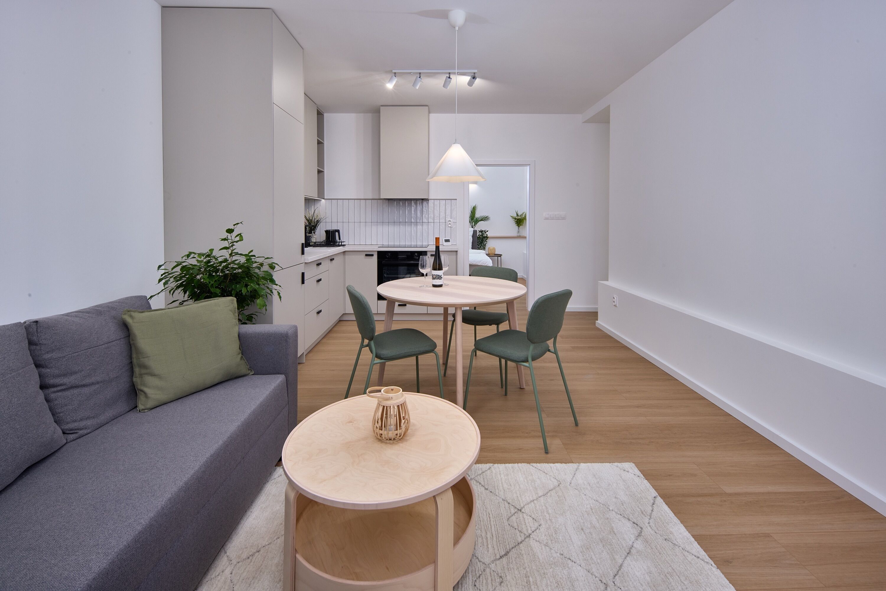 En moderne stue med sofa, et rundt bord og stole. I baggrunden er der et køkken med skabe og bordplade.