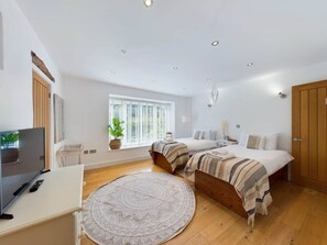 Ein Schlafzimmer mit zwei Betten, einem Fernseher, einem runden Teppich und einem Fenster mit Jalousien.
