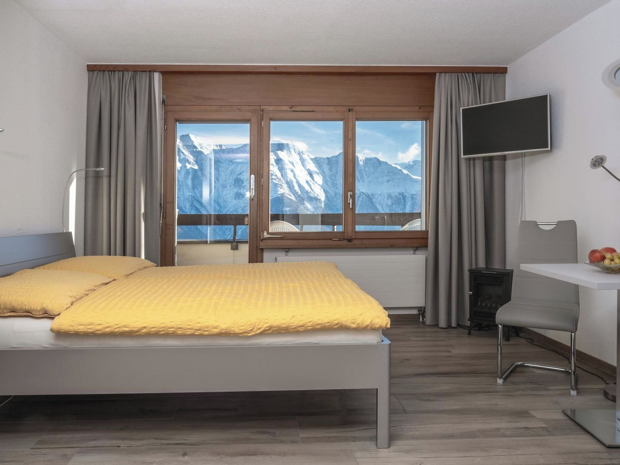 Habitación de hotel con cama, escritorio, silla, televisor y ventana con vista a la montaña.
