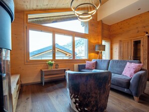 Habitació acollidora amb parets de fusta, un sofà, una banca i un gran finestral amb vista a una muntanya.