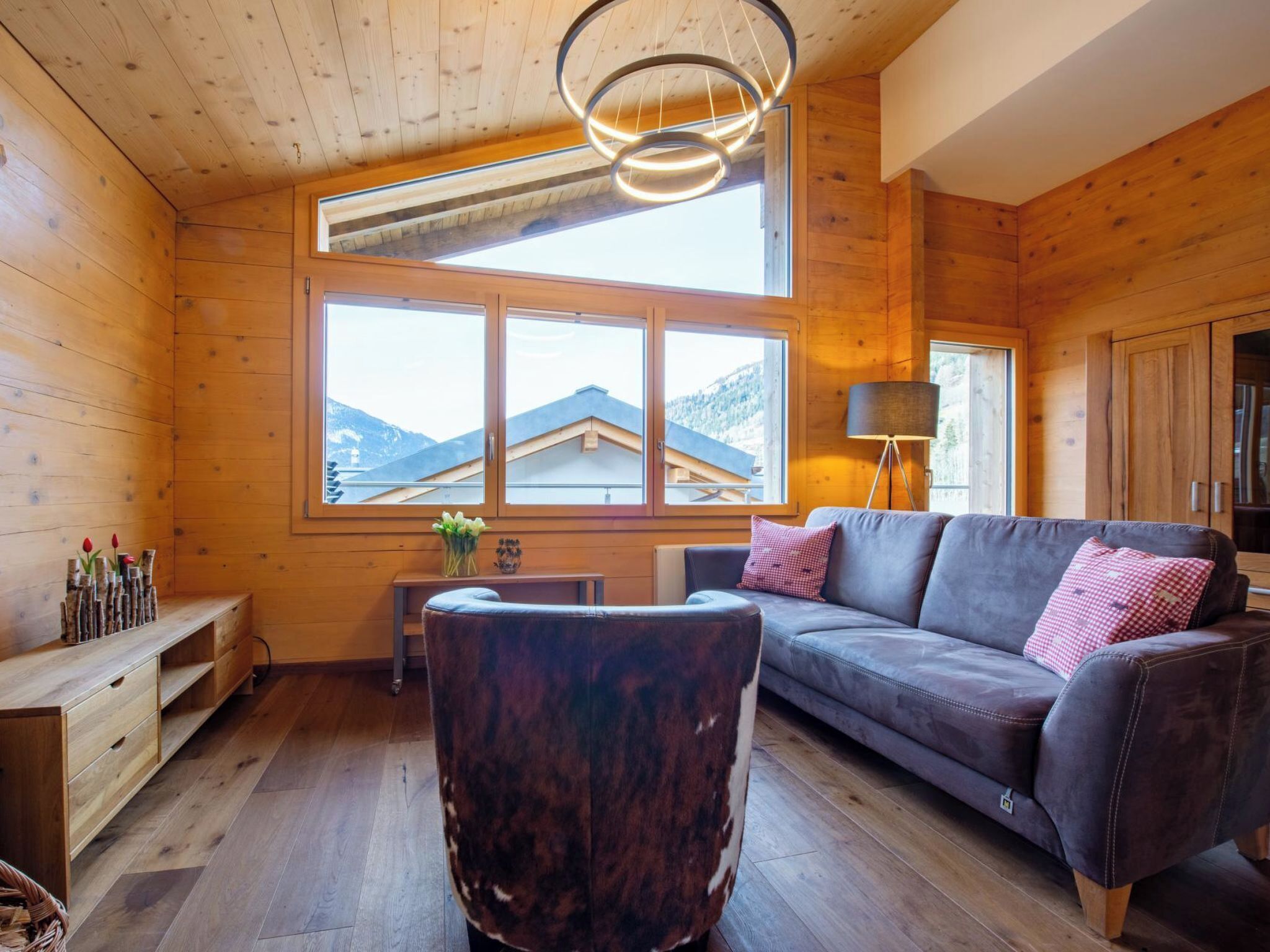 Ein Holzinterieur mit einer Couch, einer Lampe und Blick auf Berge durch große Fenster.