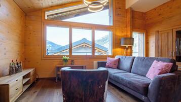 Ein Holzinterieur mit einer Couch, einer Lampe und Blick auf Berge durch große Fenster.