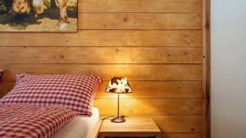 A wooden cabin-style room with a bed, a nightstand, a lamp, and a painting of cows on the wall.