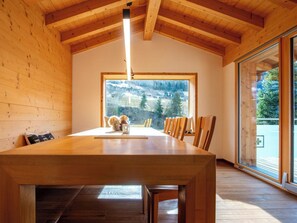 Un coin repas avec une table en bois, des chaises et une grande fenêtre donnant sur un paysage montagneux.